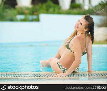 Happy young woman sitting at poolside