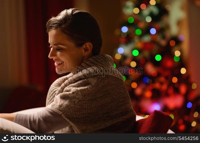 Happy young woman sitting chair in front of Christmas tree