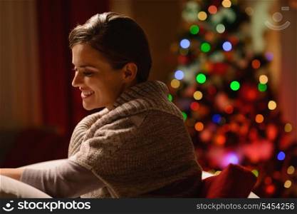 Happy young woman sitting chair in front of Christmas tree