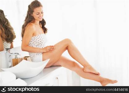 Happy young woman sitting in bathroom and examining leg