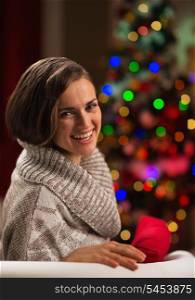Happy young woman sitting in front of Christmas tree