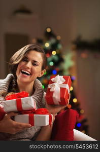 Happy young woman sitting in front of christmas tree with present boxes