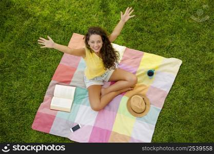 Happy young woman sitting on a blanket with arms stretched