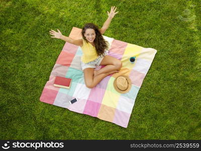 Happy young woman sitting on a blanket with arms stretched