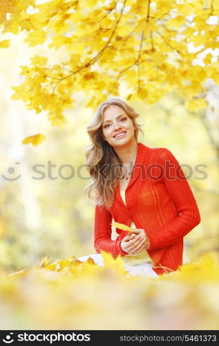 Happy young woman sitting on autumn leaves in park