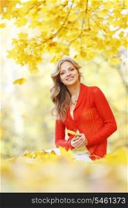 Happy young woman sitting on autumn leaves in park