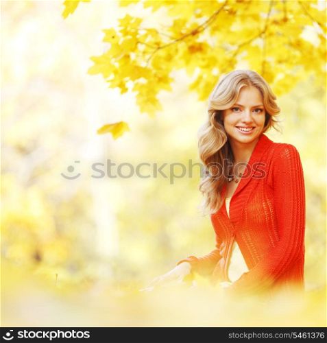 Happy young woman sitting on autumn leaves in park