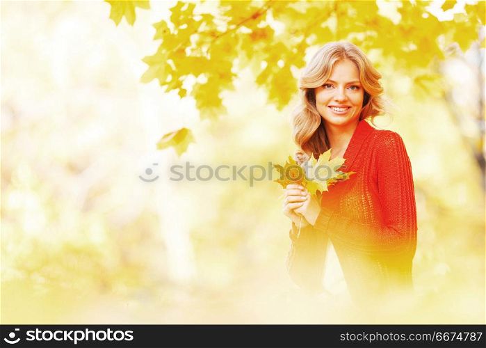 Happy young woman sitting on autumn leaves in park. Woman sitting on autumn leaves