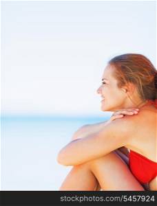 Happy young woman sitting on beach and looking on copy space