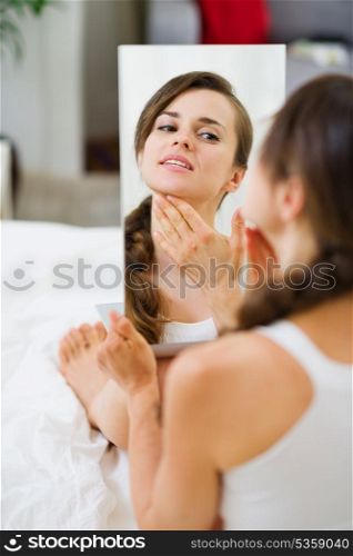 Happy young woman sitting on bed and looking on mirror