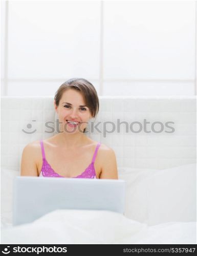 Happy young woman sitting on bed and using laptop