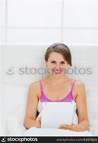 Happy young woman sitting on bed with tablet PC