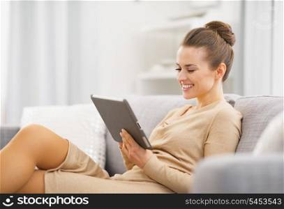 Happy young woman sitting on couch and working on tablet pc