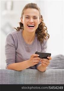 Happy young woman sitting on couch and writing sms