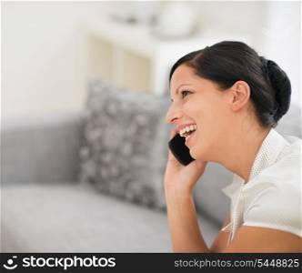 Happy young woman sitting on divan and talking mobile phone