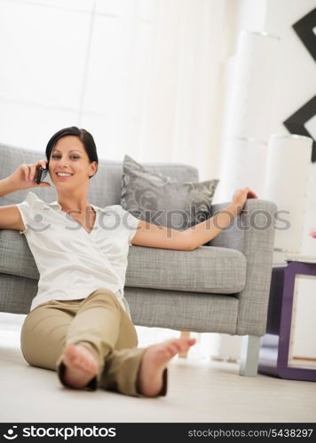 Happy young woman sitting on floor in living room and speaking mobile