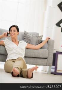 Happy young woman sitting on floor in living room and speaking mobile