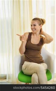 Happy young woman sitting on modern chair and pointing on copy space
