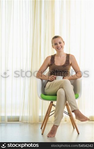 Happy young woman sitting on modern chair with cup of tea
