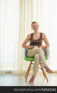 Happy young woman sitting on modern chair with cup of tea