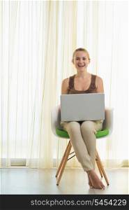 Happy young woman sitting on modern chair with laptop
