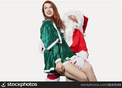 Happy young woman sitting on Santa&acute;s laps against gray background