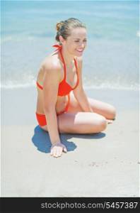 Happy young woman sitting on sea shore