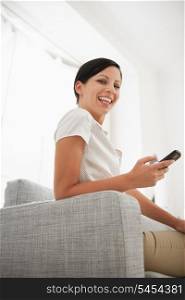 Happy young woman sitting on sofa with mobile phone