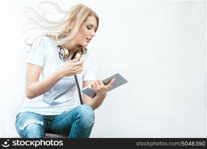 Happy young woman sitting with vintage music headphones around her neck, surfing internet on a tablet pc and smiling happily against urban city background.