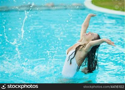 Happy young woman splashing water in pool