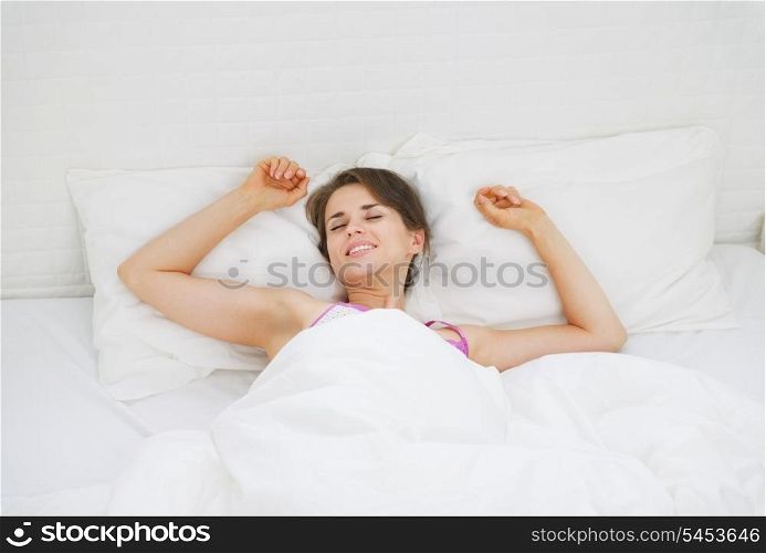 Happy young woman stretching in bed after sleep