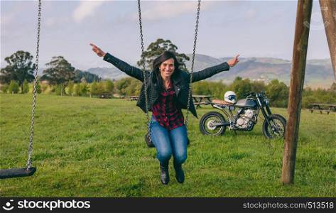 Happy young woman swinging in a recreational area with motorcycle in the background. Young woman swinging with motorcycle in the background