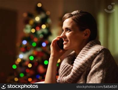 Happy young woman talking cell phone in front of christmas tree