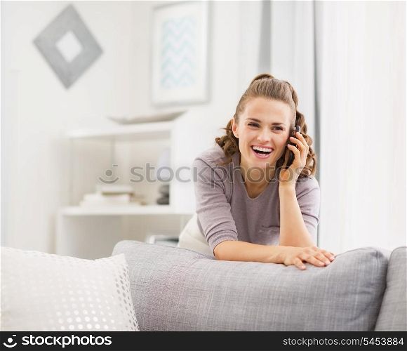 Happy young woman talking cell phone in living room