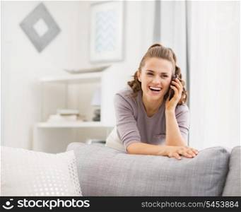 Happy young woman talking cell phone in living room