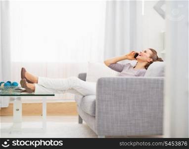 Happy young woman talking cell phone while sitting on sofa