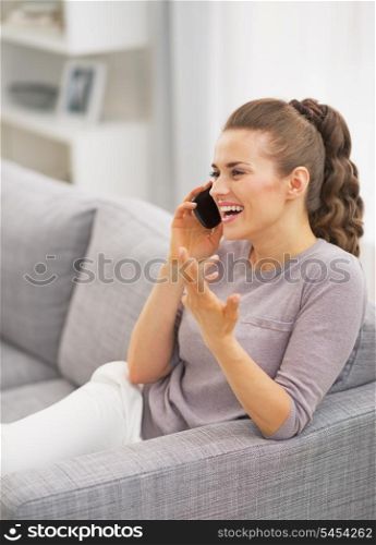 Happy young woman talking mobile phone in living room