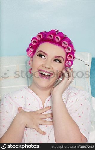 Happy young woman talking on mobile phone with hair curlers