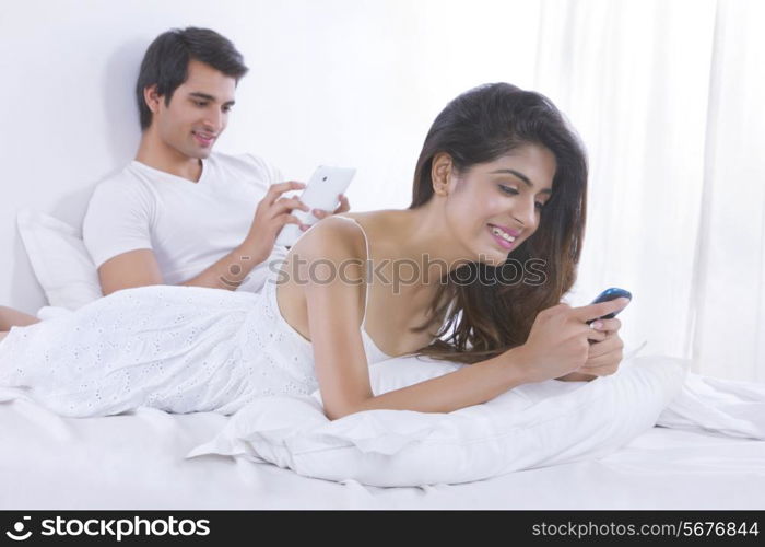 Happy young woman text messaging with man using digital in bed