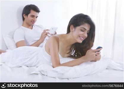 Happy young woman text messaging with man using digital in bed