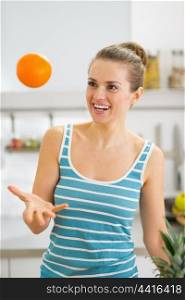 Happy young woman throwing orange in kitchen