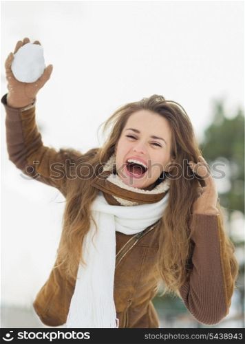 Happy young woman throwing snow ball in winter park