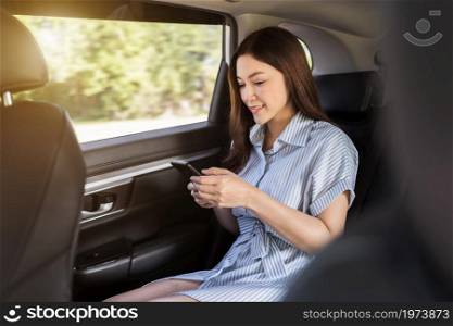 happy young woman using a smartphone while sitting in the back seat of car