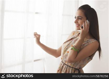 Happy young woman using cell phone by window