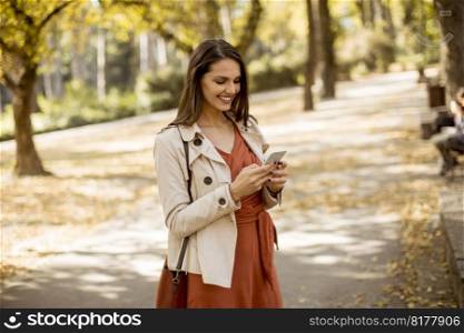 Happy young woman using cell phone in autumn park on beautiful day