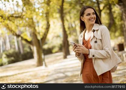 Happy young woman using cell phone in autumn park on beautiful day