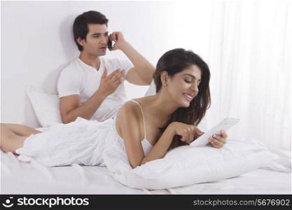 Happy young woman using digital tablet with man on call in bedroom