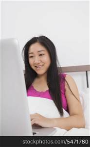 Happy young woman using laptop on bed