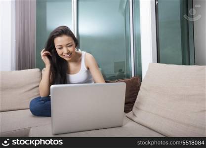 Happy young woman using laptop on sofa at home
