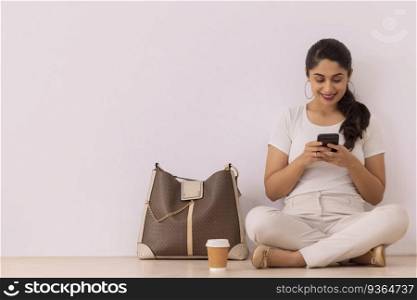 Happy young woman using Smartphone while sitting on floor